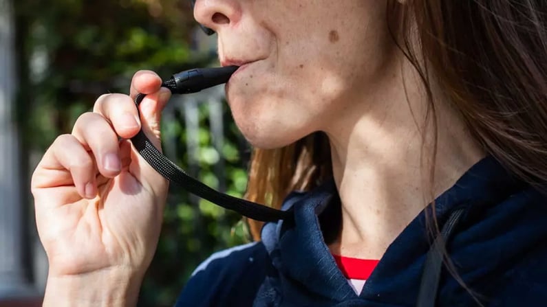 Teen using a vape hidden in a hoodie drawstring.