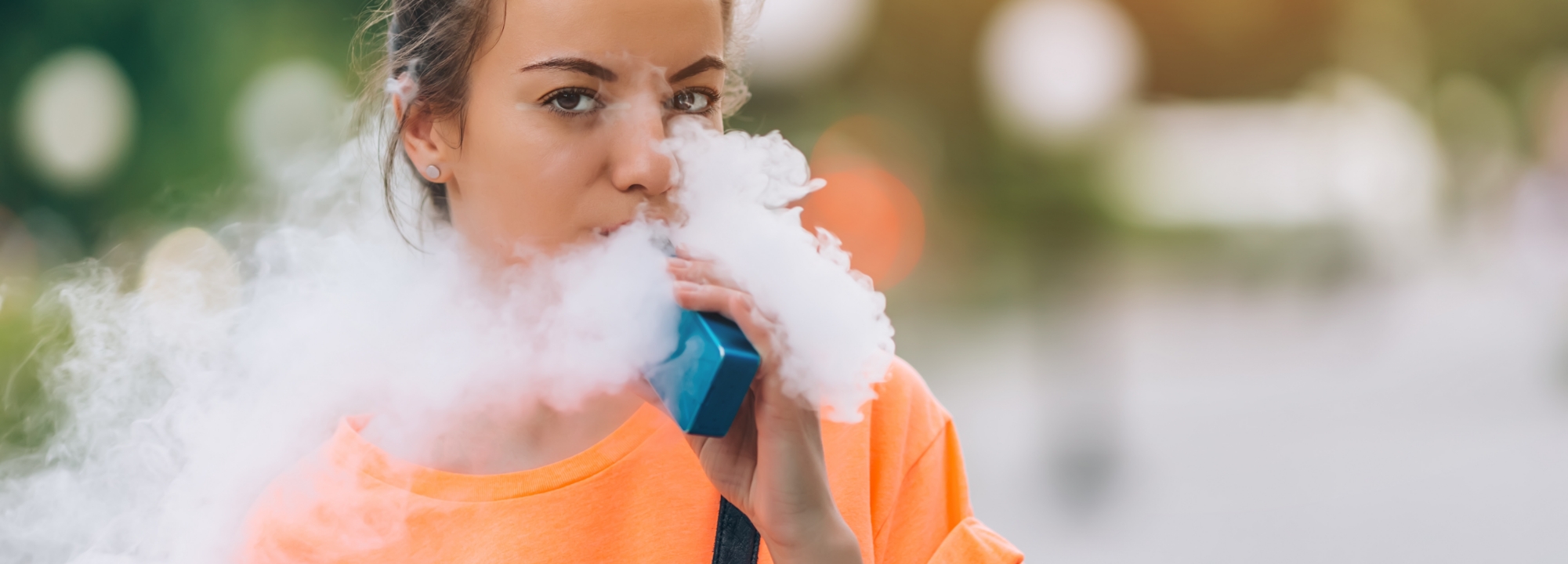 Young adult female using a vaping device and blowing vaping mist.